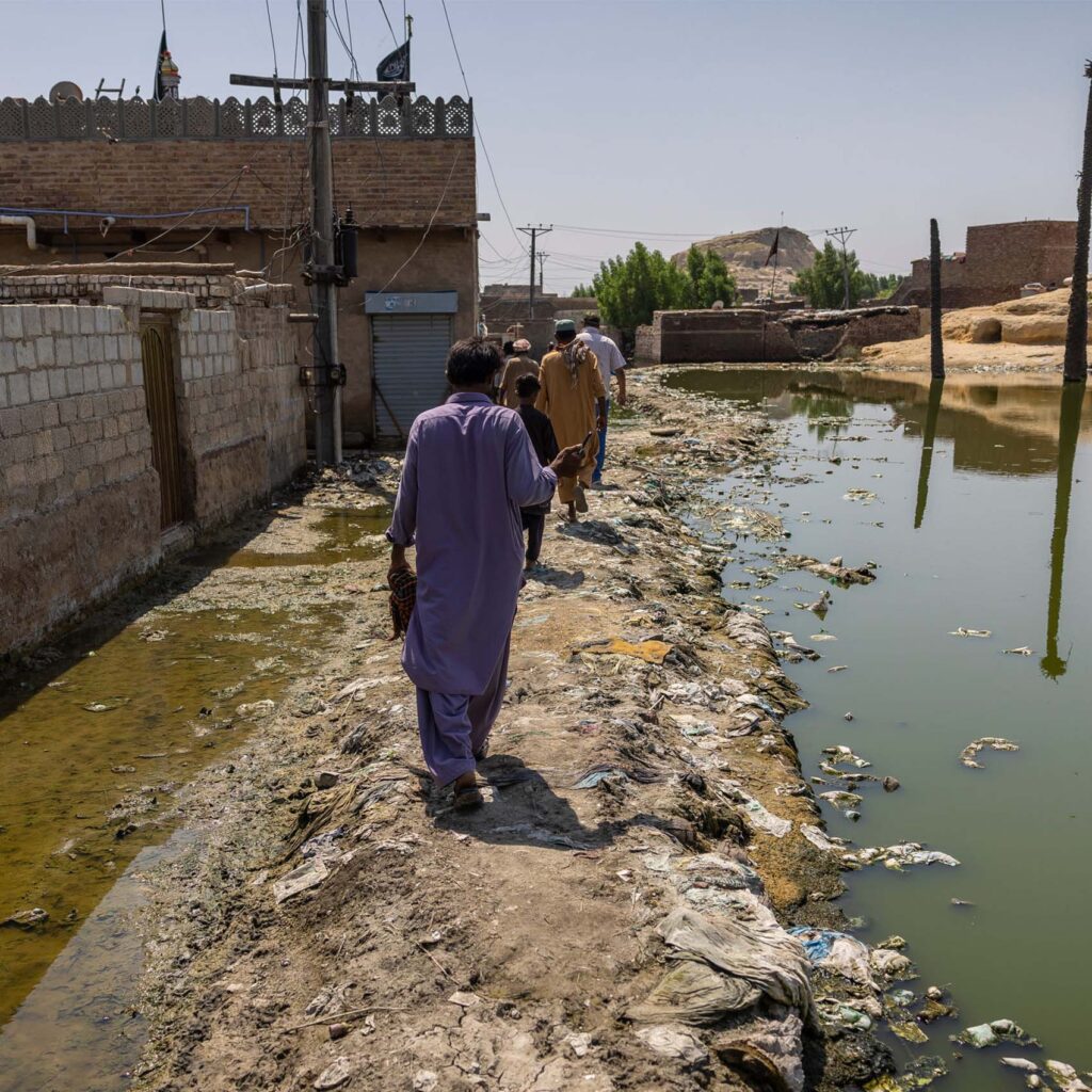 Men walking down a dirt path that is flooded on the right side in the aftermath of the devastating Pakistan floods in 2022.