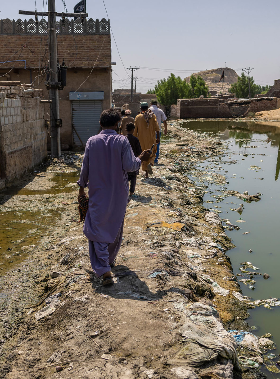 A group of people walking in a line away from the camera, next to flooded streets in Pakistan.