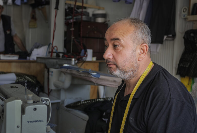 Bastami, a tailor, poses for a photo inside of his shop.