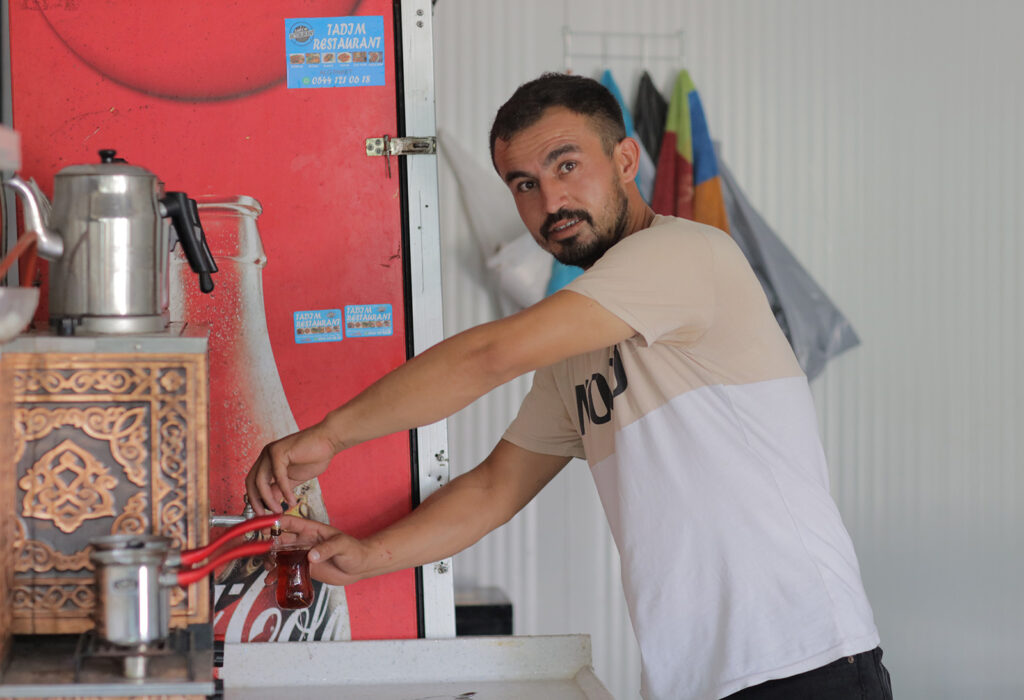 Haydar, a man wearing T-shirt reaches to clean his coffee machine.