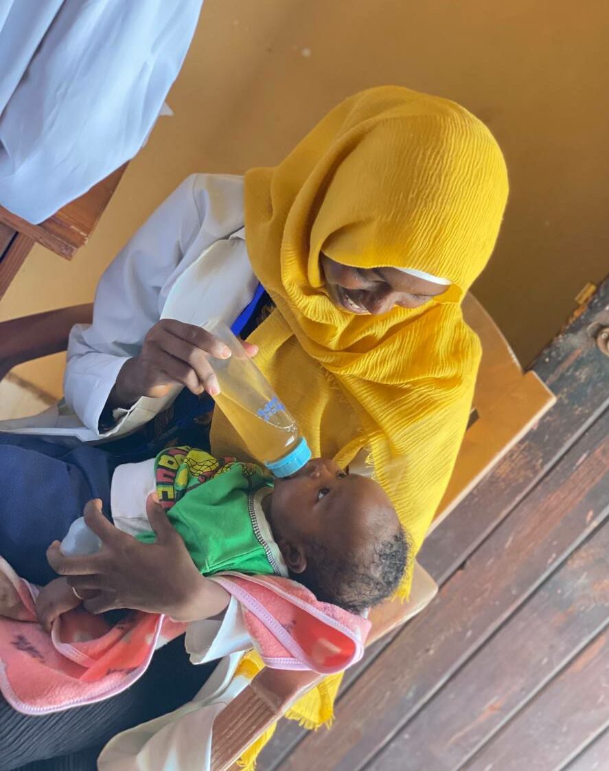 A Sudanese doctor feeds a baby with a bottle.