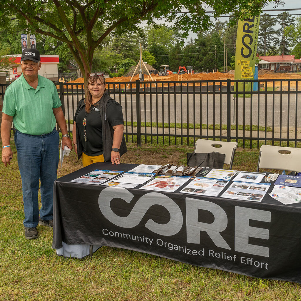 CORE NC staff stands with community member at a tabling event. Opioid and overdose educational materials displayed on table.