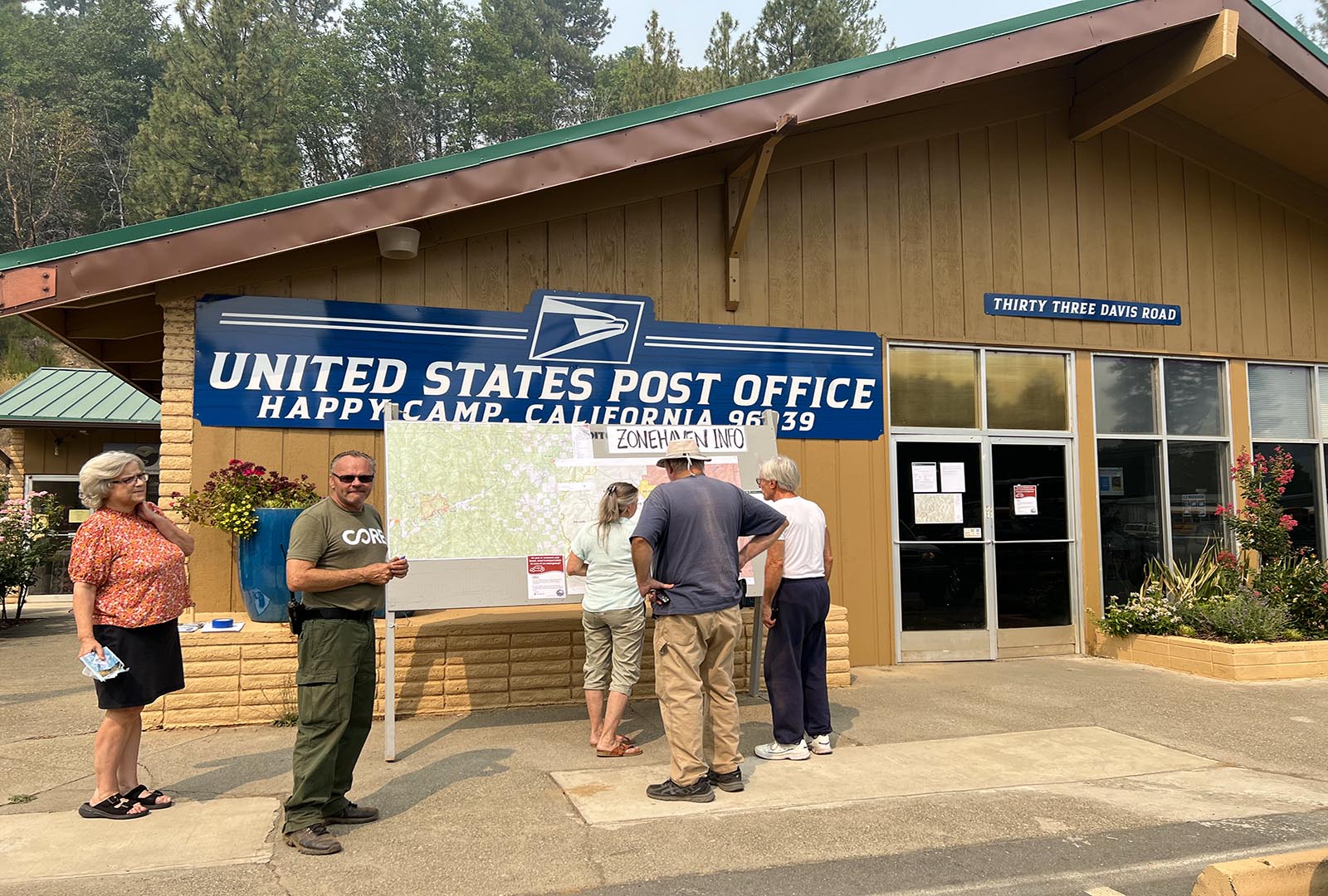 CORE staff standing outside of a post office in Siskiyou County, with a map of areas effected by a wildfire.