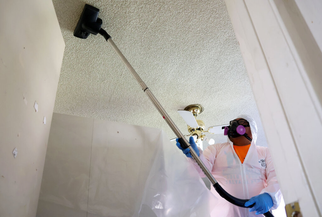 As part of CORE's smoke mitigation efforts, a worker with NDLON cleans the ceiling of an apartment with a HEPA vacuum.