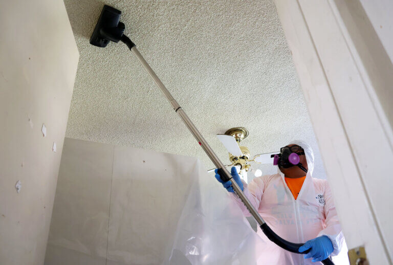 As part of CORE's smoke mitigation efforts, a worker with NDLON cleans the ceiling of an apartment with a HEPA vacuum.