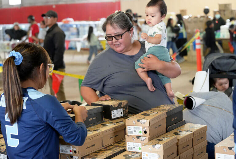 A mother is handed a pair of shoes from a volunteer.