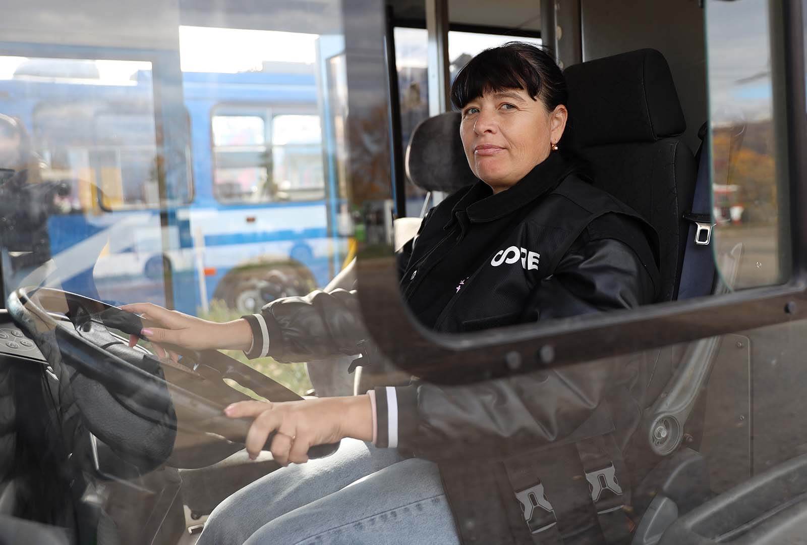 A tram driver sits in the drivers seat and poses for a photo.