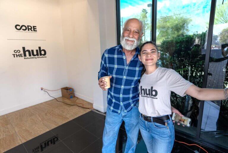 Two people pose for a photo in front of a sign for The Hub.
