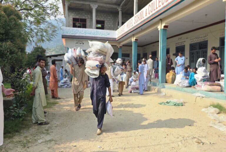 A man walks towards the camera carrying critical supplies distributed after a cloud burst event in Pakistan in 2025.
