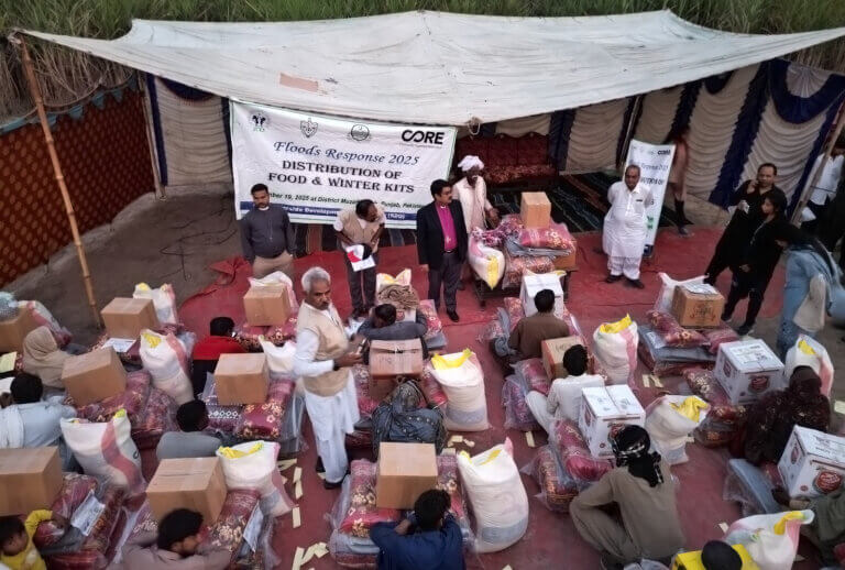 A group of people are sat in rows as they wait to receive winter kits and other supplies after a cloud burst event in August 2025