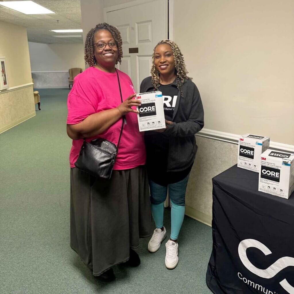 Two woman standing and smiling for a picture as one hands the other a box of N95 masks to protect from Georgia Wildfire smoke.