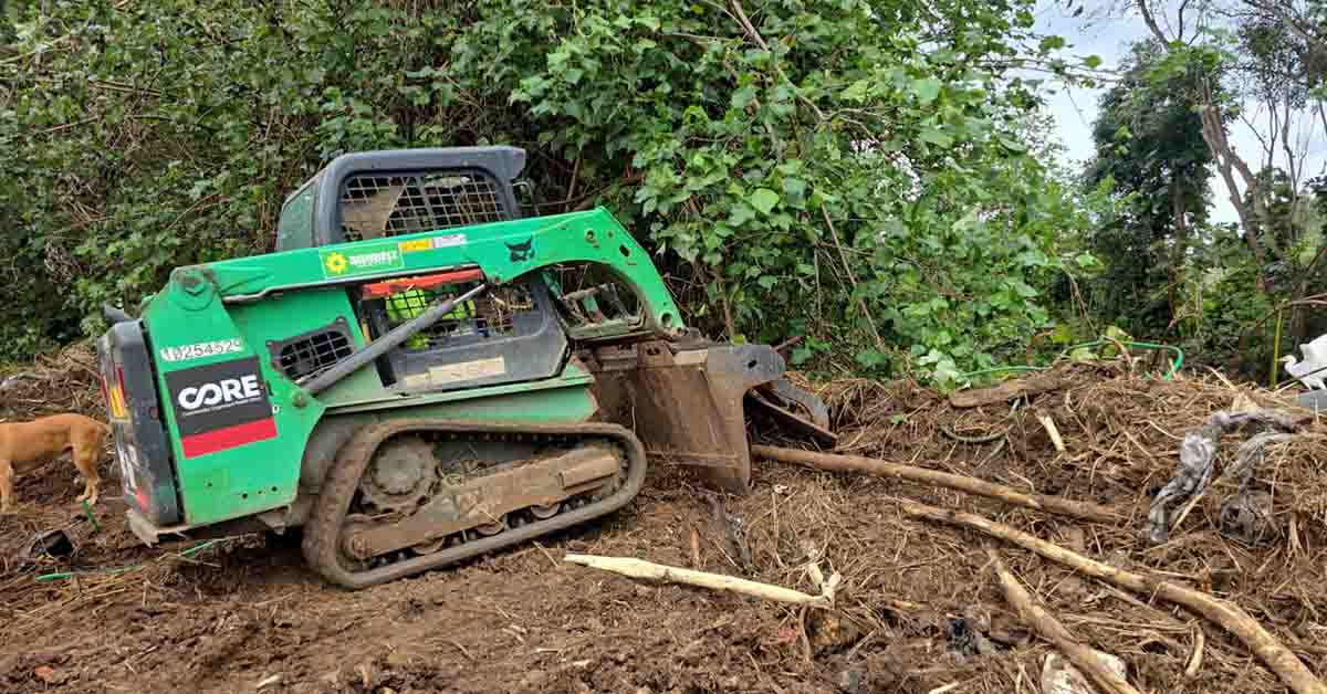 A skidsteer moving debris on a farmer in Maui after flood damage.