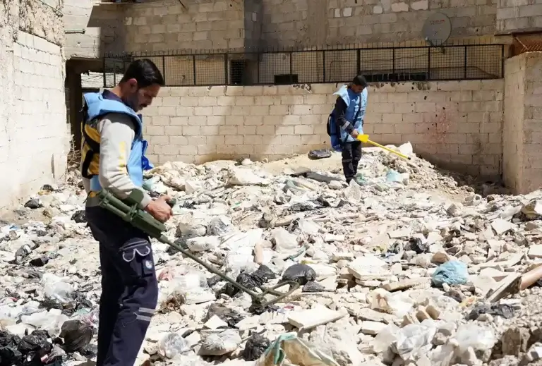 Two members of the unexploded ordnance team hold mental dectors as they walk over rubble.