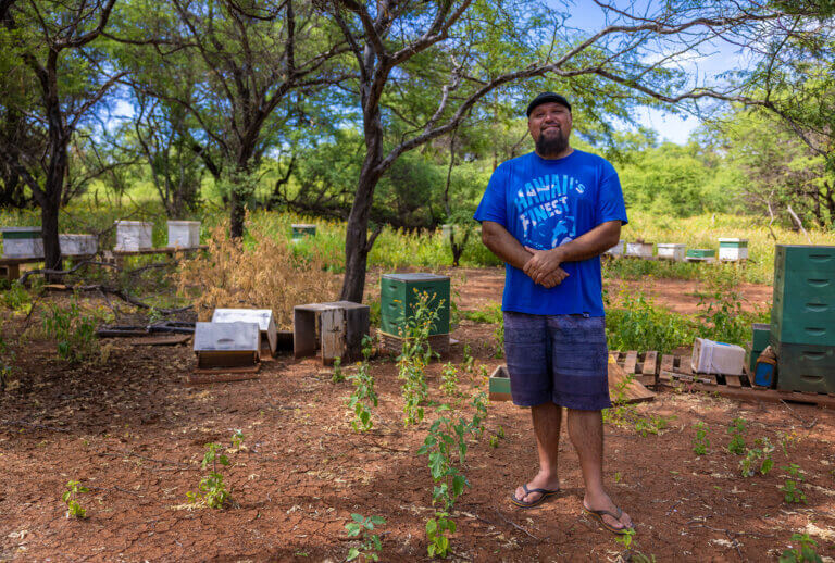 A beekeeper on Molokai, Micah, stands in front of his damaged bee boxes for a photo.