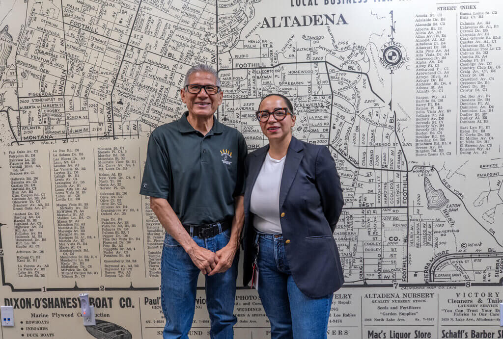 Ruben and Daniela stand for a photo infront of a wall with a map of Altadena on it.