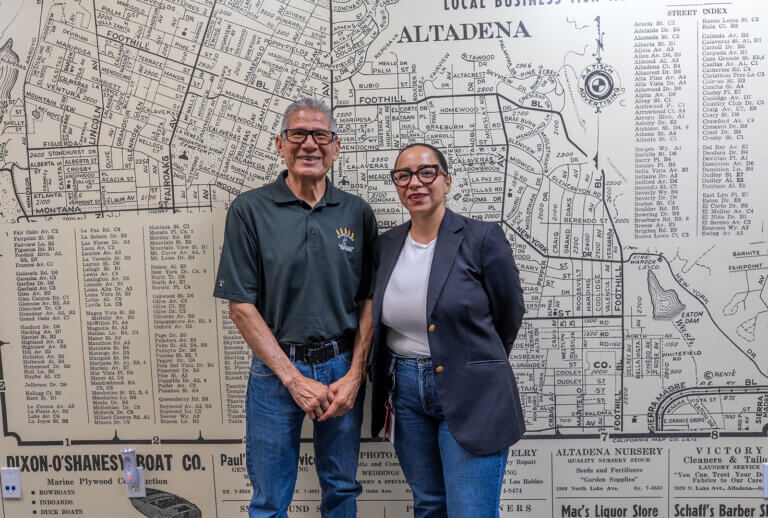 Ruben and Daniela stand for a photo infront of a wall with a map of Altadena on it.
